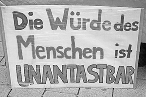 The image is a photograph of a large cardboard sign with the text Die Würde des Menschen ist UNANTASTBAR.